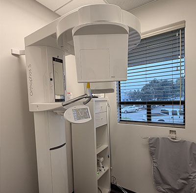 The image shows a modern medical facility with a large piece of diagnostic equipment, likely an MRI machine, inside a room with a window view of a parking lot at night.