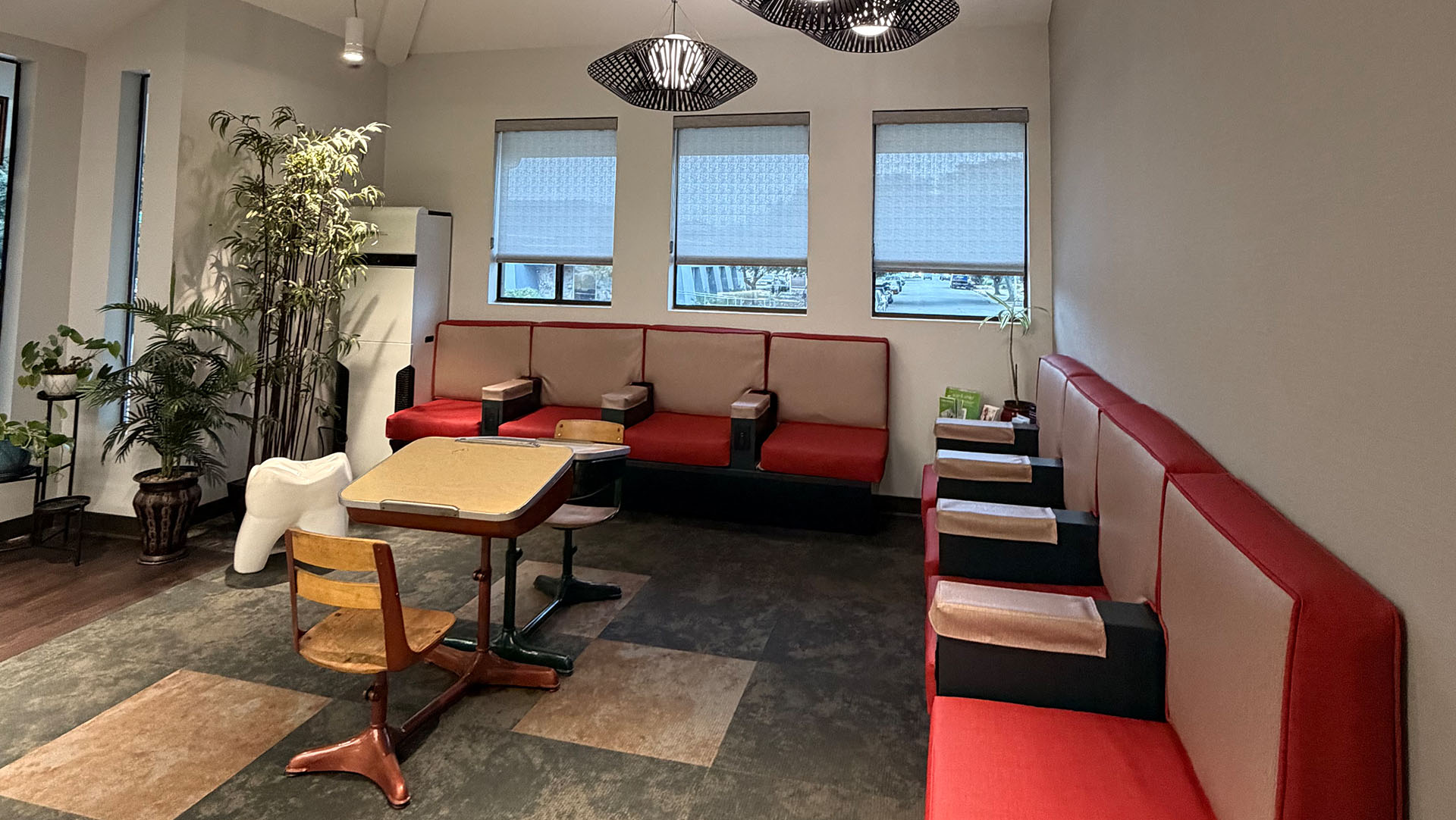 The image shows an interior space with a dining area featuring red booths and tables, a red wall, and a window with blinds partially drawn.