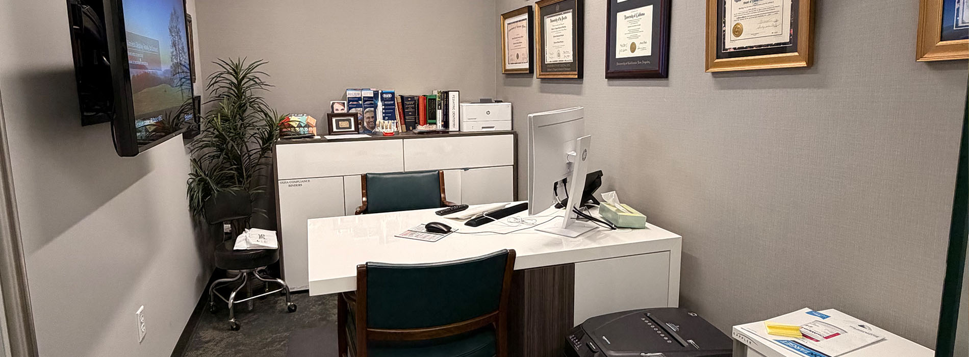 The image depicts an office setting with multiple desks, chairs, and a television screen on the wall.