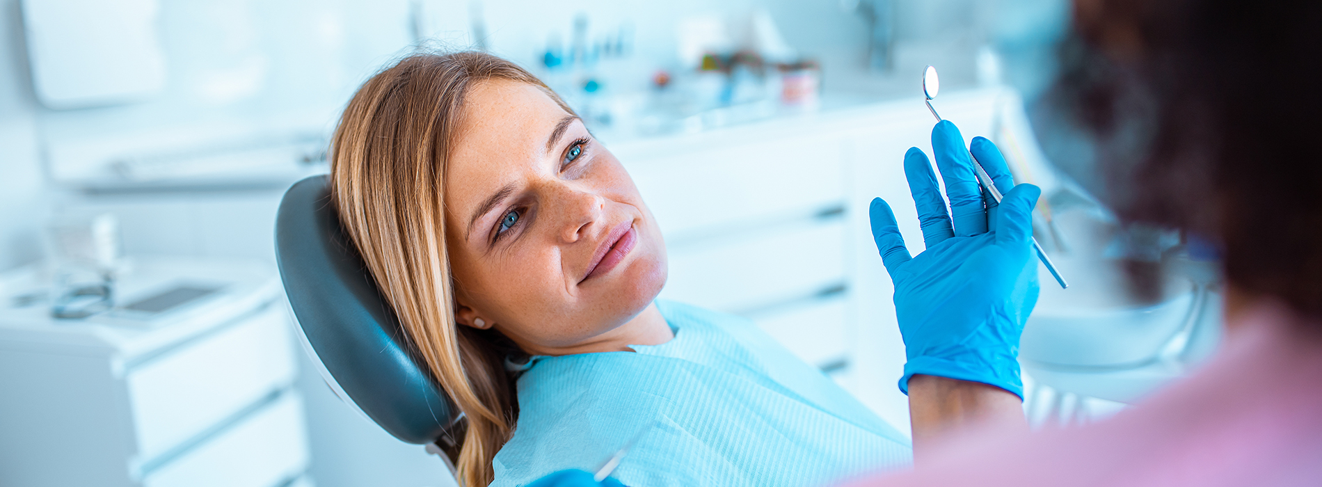 A woman seated in a dental chair with a dentist examining her teeth.