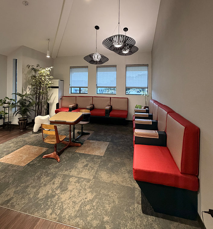 The image shows an interior space with modern furnishings, including red and blue seating areas, a dining table, and a large chandelier hanging from the ceiling.