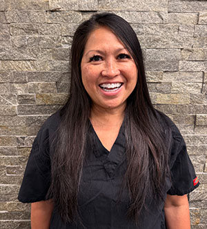 The image features a smiling woman wearing a white lab coat, standing against a backdrop of stone tiles.
