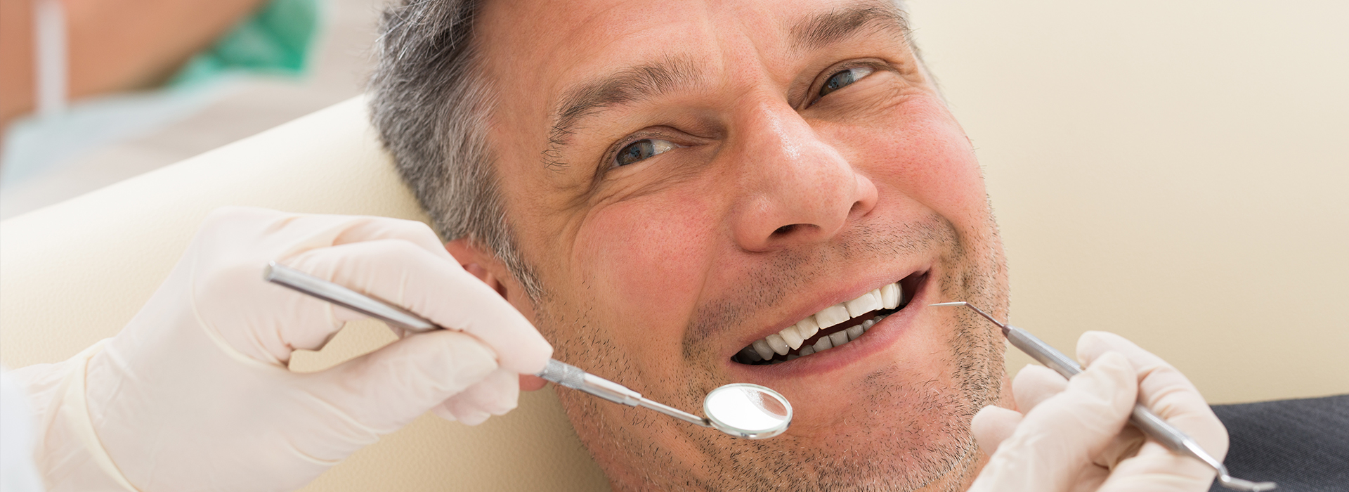 A man undergoing dental treatment, smiling while sitting in a dentist s chair with a dental hygienist working on him.