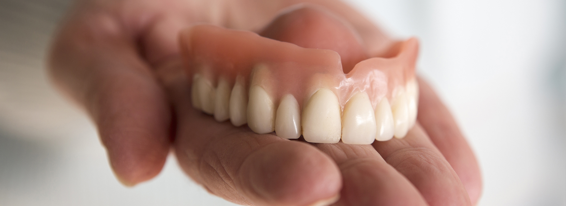 The image shows a person holding a set of dentures with a missing tooth.