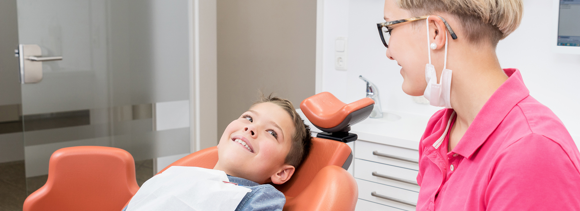 A young boy receiving dental care with an adult sitting behind him, both in a dental office setting.