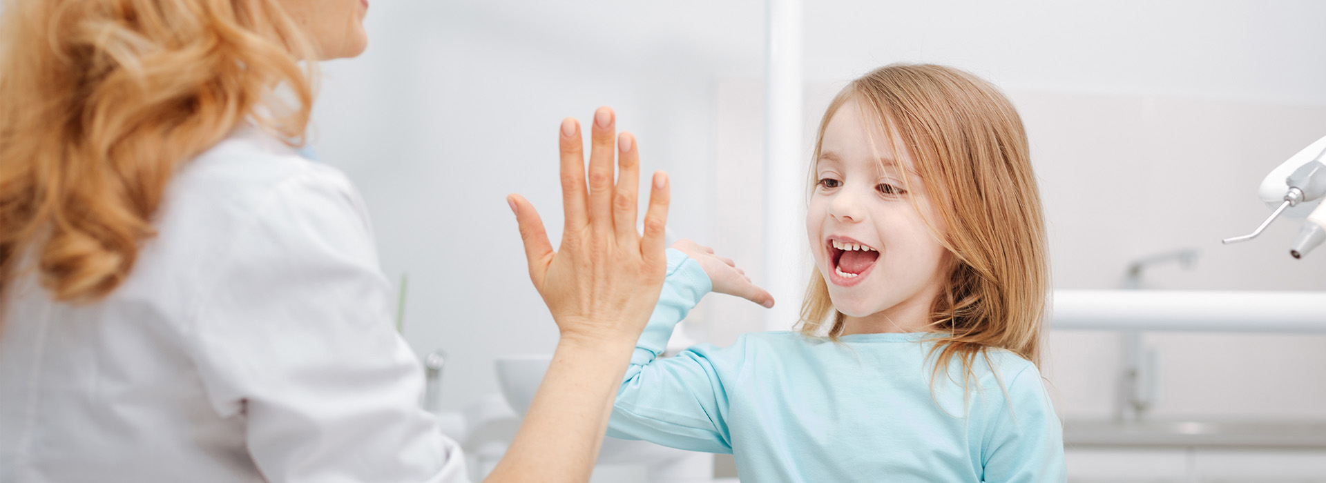 The image shows a young girl waving at the camera with her hands while standing next to an adult who appears to be washing their hands, likely in a bathroom setting.