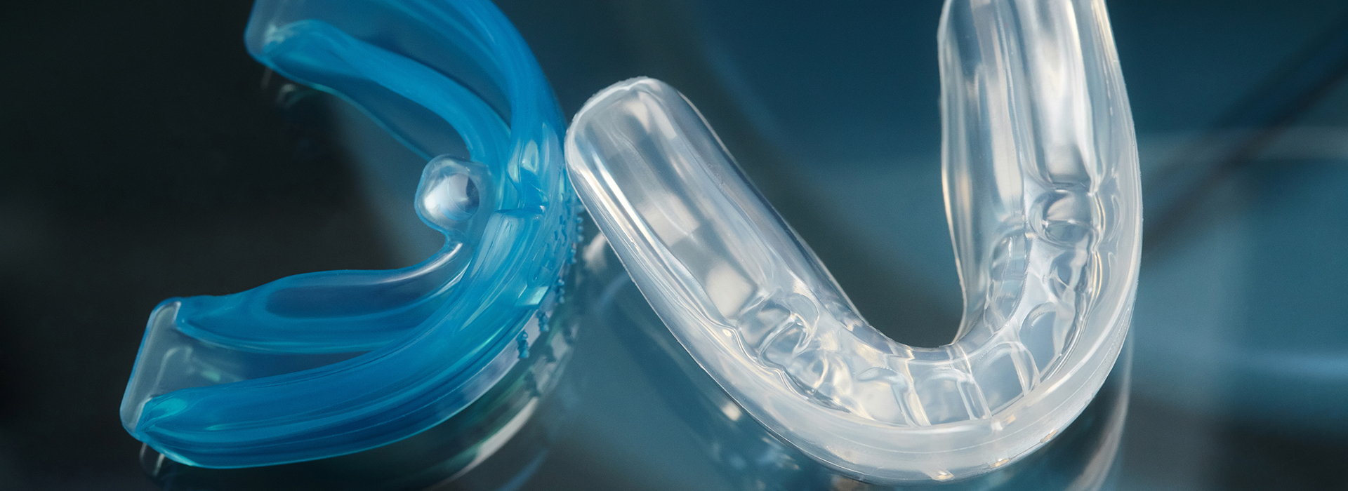 The image features a close-up of a blue dental retainer with a clear plastic hook, lying on a surface with a reflection visible beneath it.