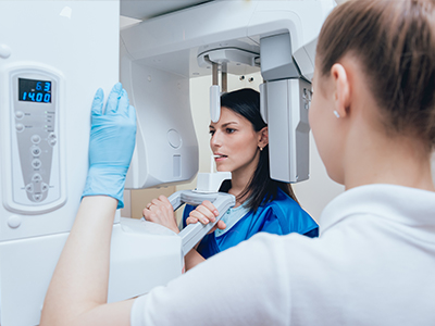 Woman standing next to large 3D scanner machine, possibly in medical or dental setting, with another person looking on.