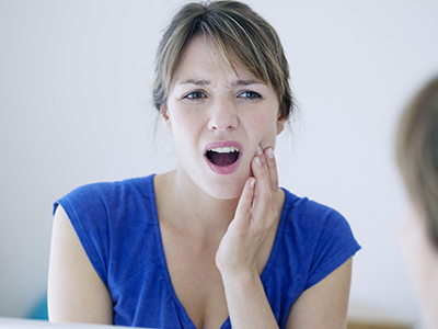 A woman with a concerned expression looking into a mirror while holding her hand to her mouth.
