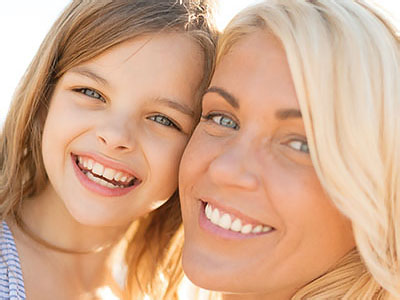 A photograph of two individuals, an adult woman and a child, smiling together with the background out of focus.