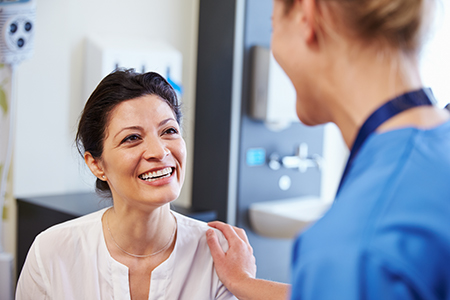 A medical professional is smiling at a patient during an examination, with a nurse standing behind them.