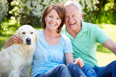 A couple sitting on grass with their golden retriever dog.