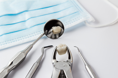 The image shows a collection of dental tools including a drill, a mirror, a probe, and other instruments, along with a tray containing a toothbrush and a small amount of toothpaste, all set against a blue cloth background.