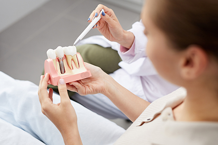 Woman holding a pink tooth model with a dental tool, possibly demonstrating dental work or training.