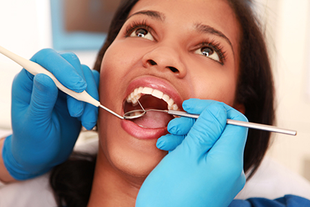 A woman receiving dental care with a wide open mouth while holding a toothbrush.