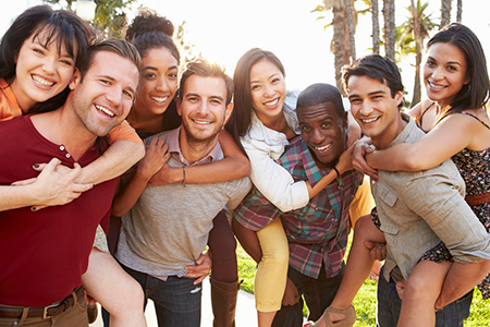 The image depicts a group of people posing together for a photograph with smiles on their faces, outdoors during daylight, likely in a casual setting.