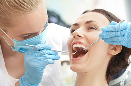 A dental hygienist performing oral care on a patient s teeth while wearing gloves and a protective mask.