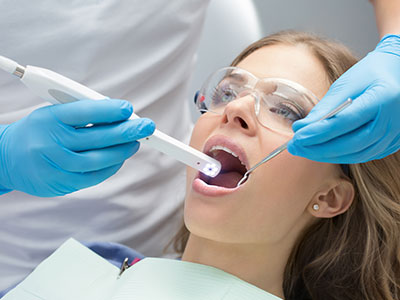 The image shows a dental hygienist using an electronic device to clean a patient s teeth during a dental appointment.