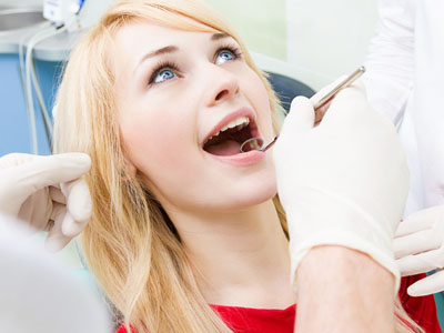 The image shows a young woman sitting in a dental chair with her mouth open, receiving dental treatment from a dentist who is working on her teeth.