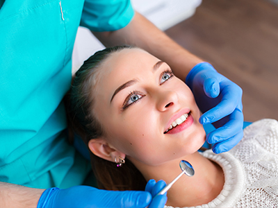 The image shows a woman receiving dental treatment from a professional, with her mouth open and a dental tool being used on her teeth.