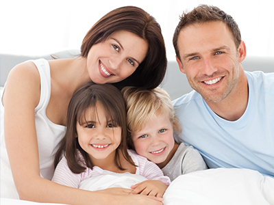 A family of four poses together on a bed with a happy expression.
