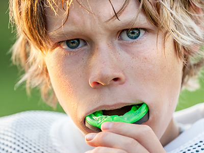 A young boy with blonde hair is blowing up a green balloon.